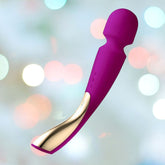 Set against a blurred backdrop of soft pastel lights, the LELO Smart Wand 2 Large Vibrating Clitoral Massager in Deep Rose promises relaxation with its rounded top and curved handle, making it a powerful tool for stress relief.